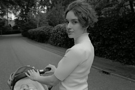 Young attractive woman walking with a stroller outdoors in a park 