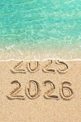 New Year concept - 2025 and 2026 written on the beach, blue ocean wave and sand