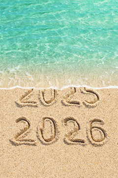 New Year concept - 2025 and 2026 written on the beach, blue ocean wave and sand