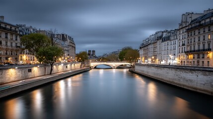 Fototapeta premium Serene twilight view of a river flowing under a bridge, flanked by illuminated buildings