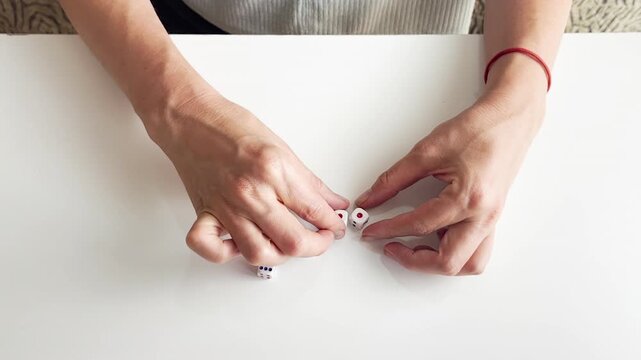 Close up video of a woman playing a dice game on a white table. Rolling cubes with numbers, chance, gambling, board game elements, luck and entertainment concept