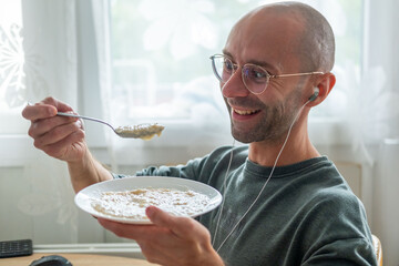 Young man eating oatmeal while working computer desk, multitasking breakfast with healthy food during busy office routine, combining nutrition and productivity lifestyle, professional modern lifestyle