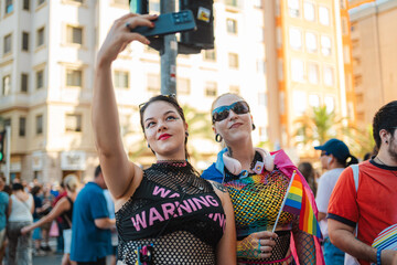 Two women taking a selfie at pride parade with rainbow flag