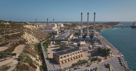 Malta: Aerial shot capturing Delimara Power Station, Malta's main electricity source, featuring industrial structures, chimneys, and storage tanks along the coast. Drone flight