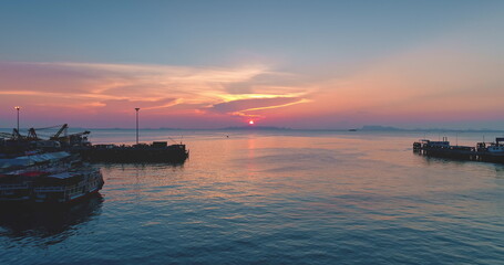 Tranquil seascape at sunset with colorful sky reflecting on the calm water of the Gulf of Thailand, with silhouettes of piers, boats, and cranes creating a peaceful and scenic view