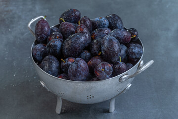Bowl filled with fresh plums on a dark surface