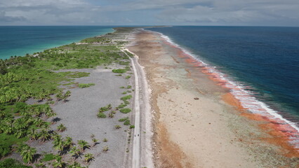 French Polynesia, Rangiroa island: Aerial view capturing Tiputa motu's road dividing Rangiroa lagoon and Pacific Ocean, featuring vibrant corals and white sand beaches. Drone flight