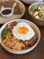 An inviting close-up shot of a gourmet bowl, capturing the vibrant textures of tender grilled medium-rare beef, aromatic beef fat fried rice, and a glistening sunny-side up egg. A truly savory dish.