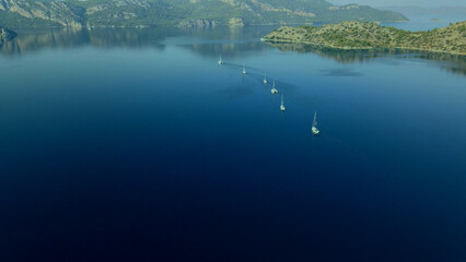 An aerial view of a group of sailing yachts leaving the strait for the open sea early in the morning
