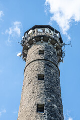 Svatobor lookout tower stands tall with its rugged stone structure and communication equipment. Clear skies enhance the scenic view, inviting visitors to explore the surroundings.