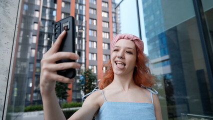 A teenage girl poses for a selfie on her smartphone. She shows her pierced tongue to her friends