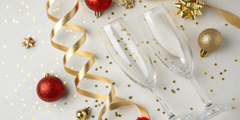 Two empty champagne flutes on white surface with golden ornaments, ribbons and star shaped confetti for festive holiday celebration and seasonal design purposes