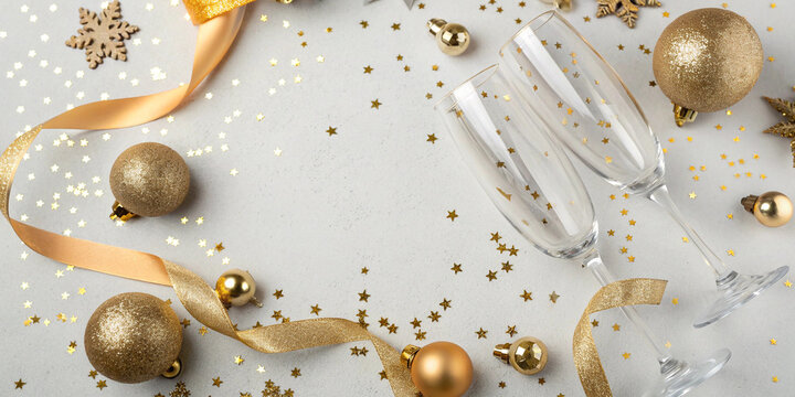 Two empty champagne flutes on white surface with golden ornaments, ribbons and star confetti for new year or christmas celebration and festive seasonal design projects - Powered by Adobe
