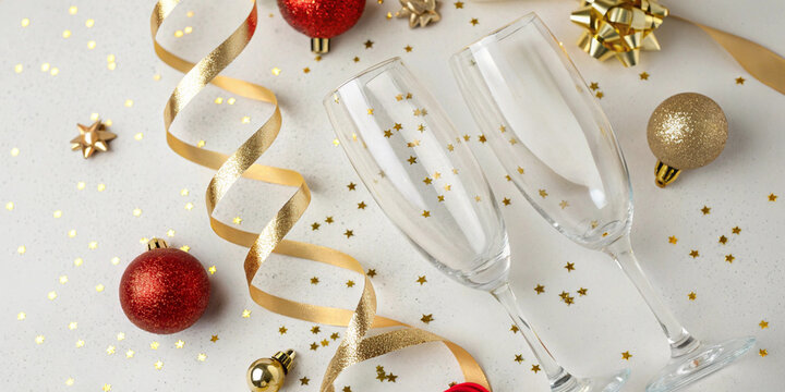 Two empty champagne flutes on white surface with golden ornaments, ribbons and star shaped confetti for festive holiday celebration and seasonal design purposes - Powered by Adobe