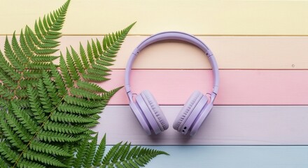 Purple headphones resting on a pastel striped background with a fern leaf.