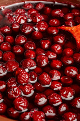 Preparing freshly picked red cherries with sugar to make cherry jam in a saucepan with a wooden spoon, closeup. Cooking berries marmalade, home cooking