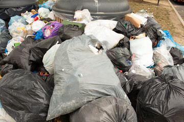 Heap of garbage bags piled around large bins at a highway rest area. Plastic waste and discarded...