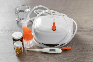 Close-up of a medical nebulizer with inhalation mask, digital thermometer, and medicine bottles on...