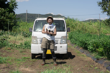 軽トラの前で収穫した野菜を持つ笑顔でカメラ目線女性 農業や農作業の全身