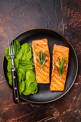 Grilled salmon fillet with spinach, fish steak in a plate. brown background. top view