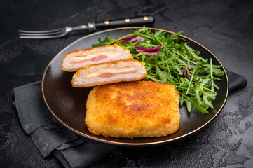 Chicken cordon bleu cutlet with cheese and ham on plate with salad. black background. top view