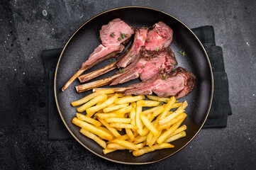 Roast lamb cutlets, mutton meat steaks on plate with french fries. black background. top view