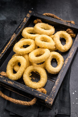Raw squid rings with breading, uncooked calamari snack. black background. top view