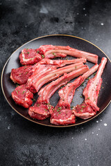 Fresh mutton chops, raw lamb meat cutlets on a plate. black background. top view