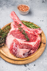 Uncooked tomahawk steak, raw black angus beef rib eye with bone on wooden board. grey background. top view