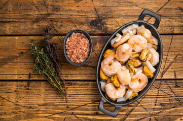 Ready for cooking fresh Raw Seafood Cocktail with Mussels, Clams, Prawns, Shrimps and squid in skillet. wooden background. top view