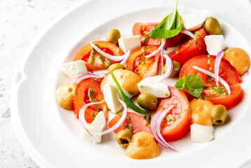 Fresh salad with tomatoes, mozzarella, olives, red onion, spinach, and creamy dressings on a white...