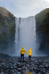 Obraz premium Couple exploring the stunning Skogafoss waterfall in Iceland during a misty afternoon