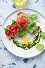 Plate with tomato bruschettas and basil oil on a white and blue granite background, vertical shot, middle close-up, high angle view