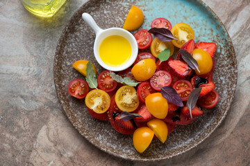 Plate with fresh strawberry, tomato and basil salad on a brown granite background, horizontal shot, high angle view