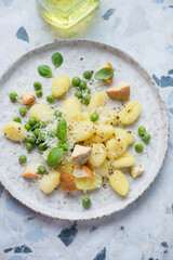 Plate of italian gnocchi served with cheese and green peas, vertical shot on a white and blue granite surface, elevated view