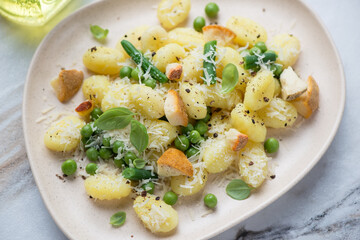 Potato gnocchi served with different cheese, green peas and basil on a beige plate, middle closeup, horizontal shot