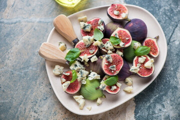 Plate with fresh fig fruits and blue cheese on a beige and grey granite background, horizontal shot, elevated view