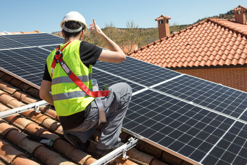 Man installs solar panels on a rooftop under a clear blue sky during daylight hours in a...