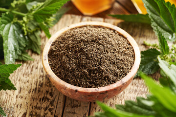 A bowl of stinging nettle seeds with fresh leaves on a table