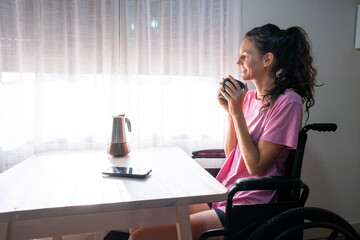Young woman in wheelchair enjoying morning coffee by window