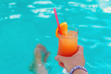Cocktail in hands of woman against the background of swimming pool. Selective focus.