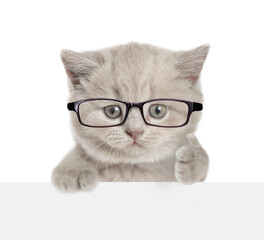 Funny smart kitten wearing eyeglasses looks above blank white banner and shows thumbs up gesture. isolated on white background