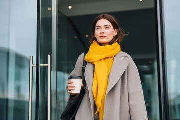 Confident young woman arriving at office on a rainy autumn morning with coffee in hand. Modern business lifestyle captured through bright seasonal fashion and calm urban routine