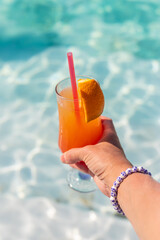 Cocktail in hands of woman against the background of swimming pool. Selective focus.