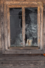 Old wooden window with cracked panes reflecting a faint silhouette in a weathered rustic cabin. Spring hiking in Carpathian mountains, Ukraine