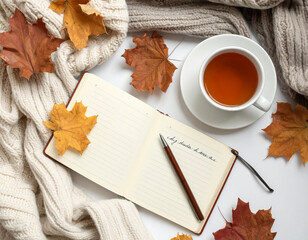 Flat lay of autumn journal with handwritten notes, cup of tea, dried leaves, cozy blanket, natural light, creative workspace photography