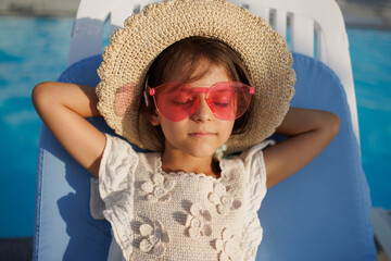 little girl in hat and glasses relaxing near the pool.