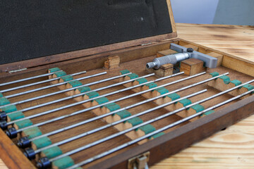 A set of vintage depth micrometers is displayed in an open wooden case on a rustic wooden table. The precise measuring tools with their various extension rods.