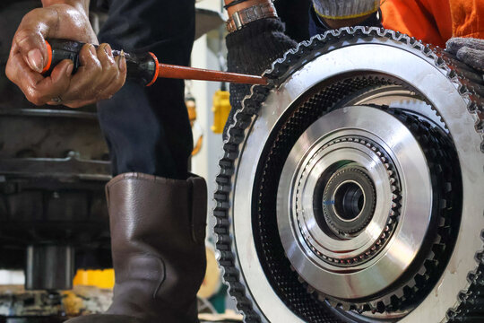 Close-up mechanic's hands working on a large, remove the retaining ring with a screwdriver. Dismantle rotating clutch allison transmission. Workplace.