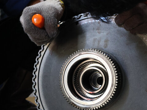 Close-up mechanic's hands working on a large, remove the retaining ring with a screwdriver. Dismantle rotating clutch allison transmission. Workplace.